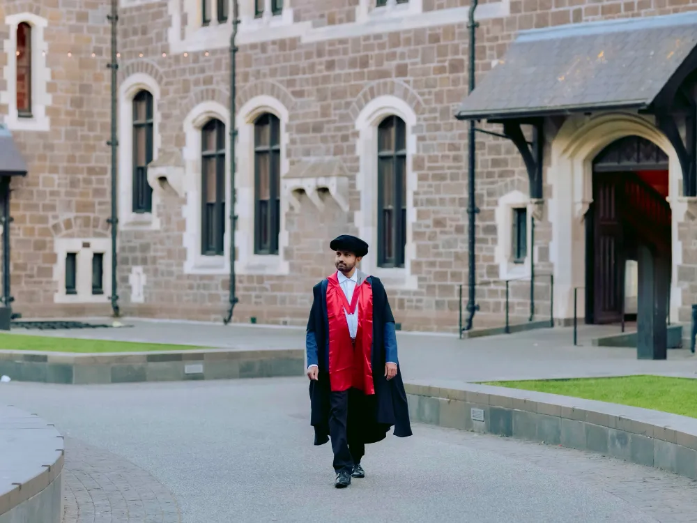 Dr. Yasas Sri Wickramasinghe in doctoral robes walking across a stone quadrangle in Christchurch on his PhD graduation day