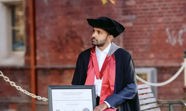 Dr. Yasas Sri Wickramasinghe in doctoral robes, sitting on a bench with his University of Canterbury PhD certificate