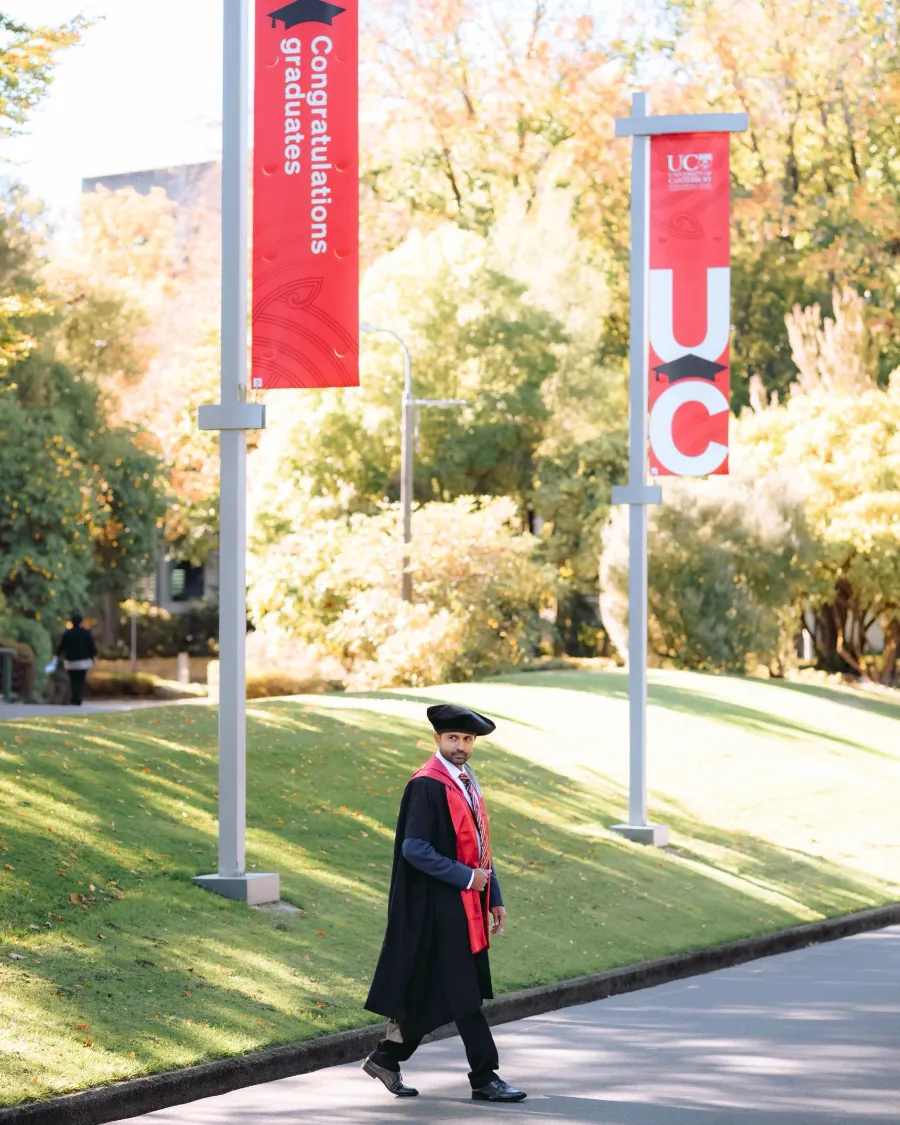 Dr. Yasas Sri Wickramasinghe in doctoral robes beneath University of Canterbury graduation banners