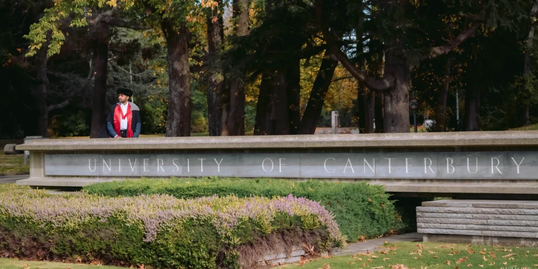 Dr. Yasas Sri Wickramasinghe in doctoral robes at the University of Canterbury entrance sign