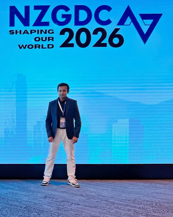 Yasas standing in front of the NZGDC 2026 ‘Shaping Our World’ backdrop, with the Auckland skyline behind him