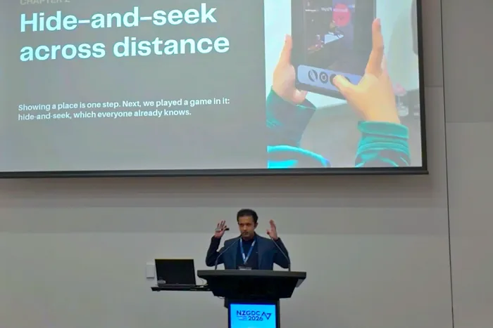Mid-explanation at the lectern, in front of the ‘Hide-and-seek across distance’ chapter slide