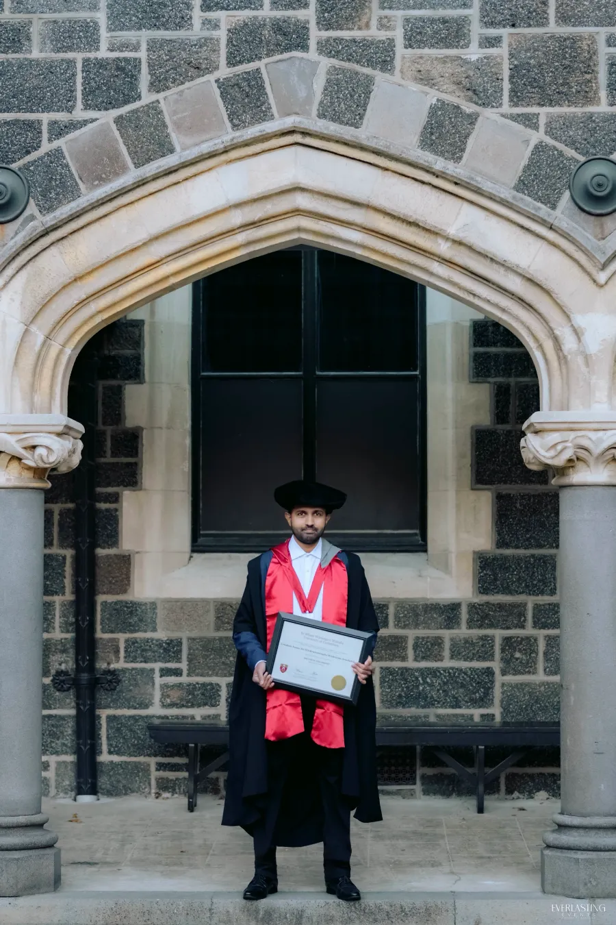 Dr. Yasas Sri Wickramasinghe holding his University of Canterbury PhD certificate beneath a stone archway